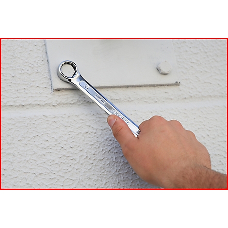 Eine Hand hält einen Schraubenschlüssel, um eine Schraube zu lösen. Der Schraubenschlüssel liegt auf einem weißen Untergrund.